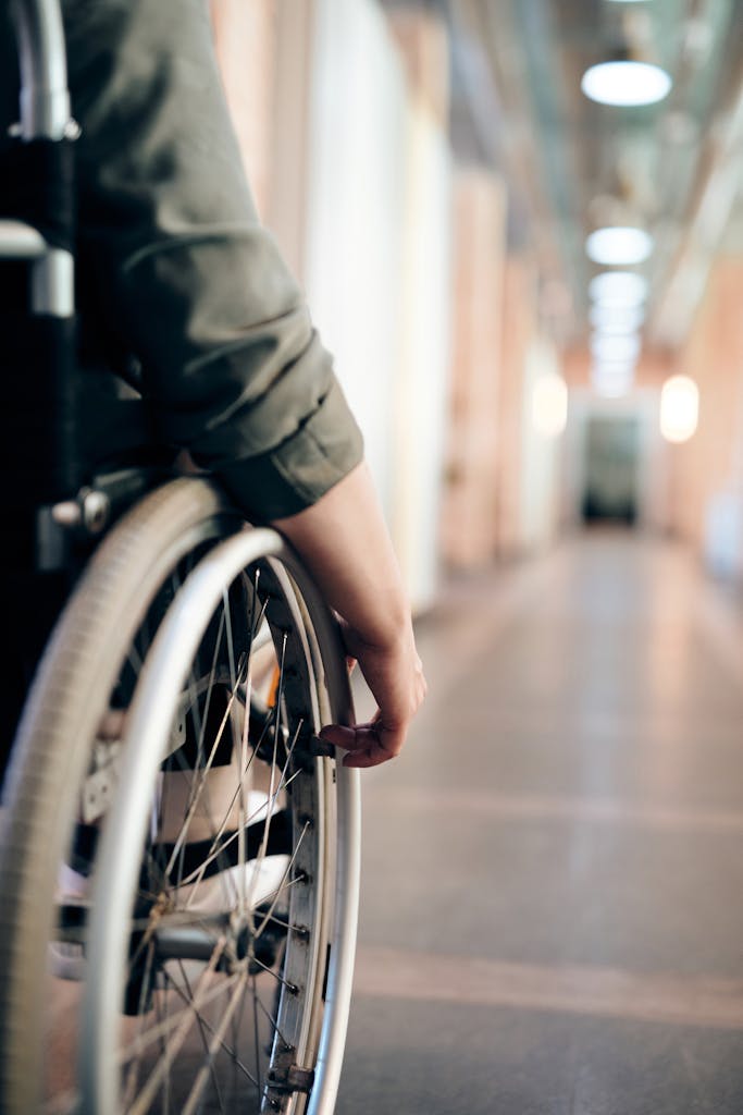A person in a wheelchair is navigating an indoor hallway, focus on the wheel and hand.