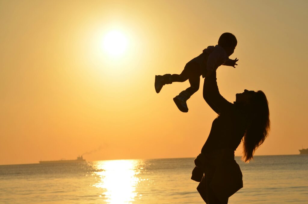 Silhouette of a mother lifting her child at a sunset beach, capturing warmth and love.