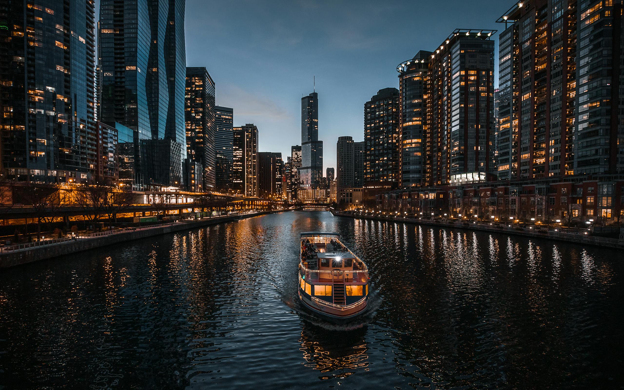 Stunning view of Chicago's skyline at dusk with reflections on the river and a boat cruising.
