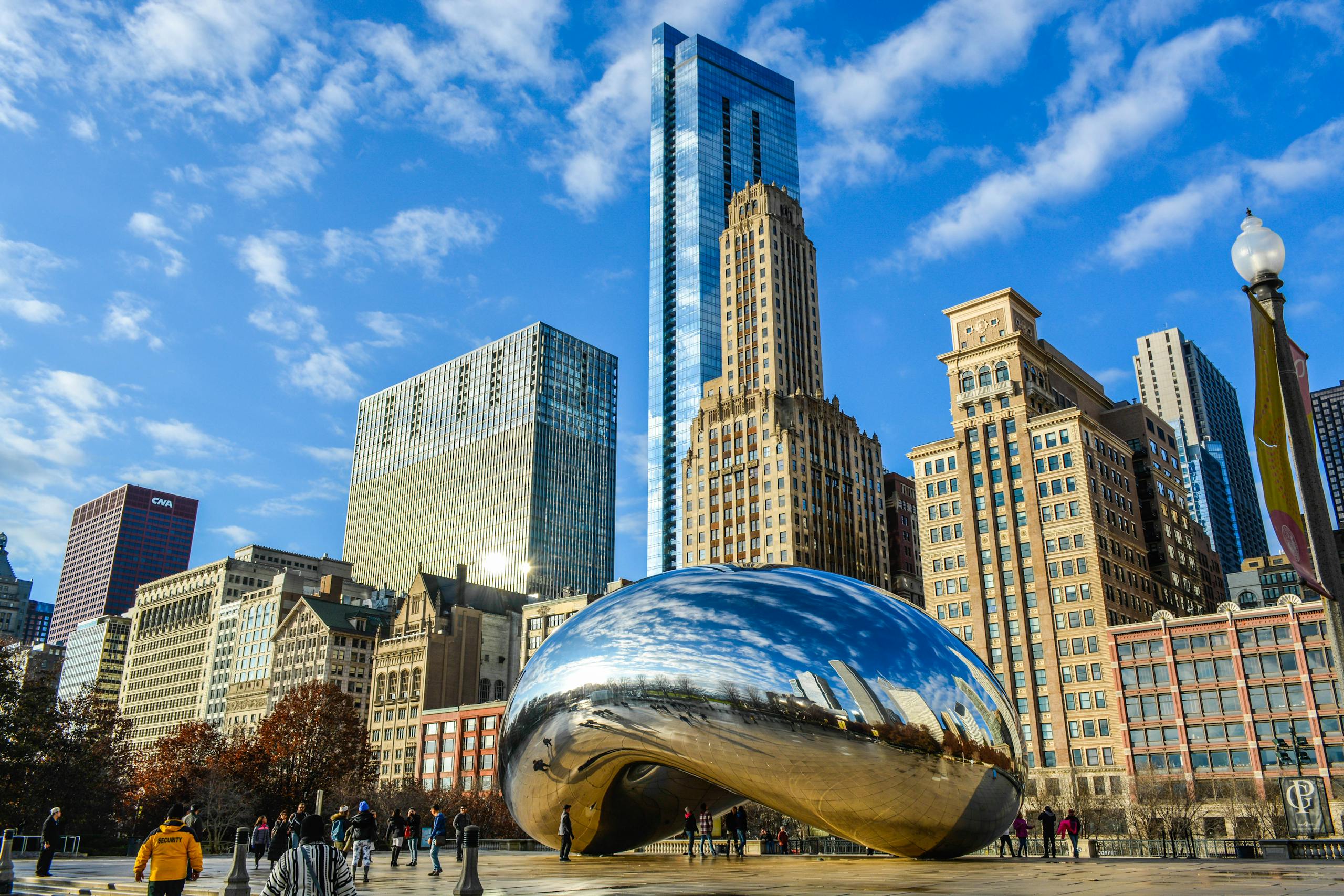 View of the iconic Cloud Gate sculpture in Chicago's Millennium Park with city skyscrapers in the background.